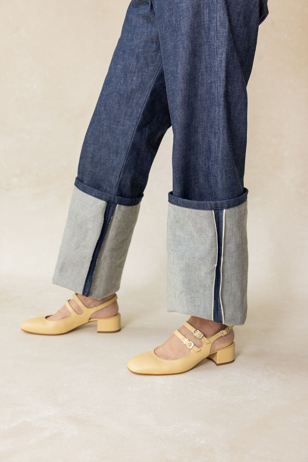 Person wearing blue and gray pants with yellow shoes on a beige background