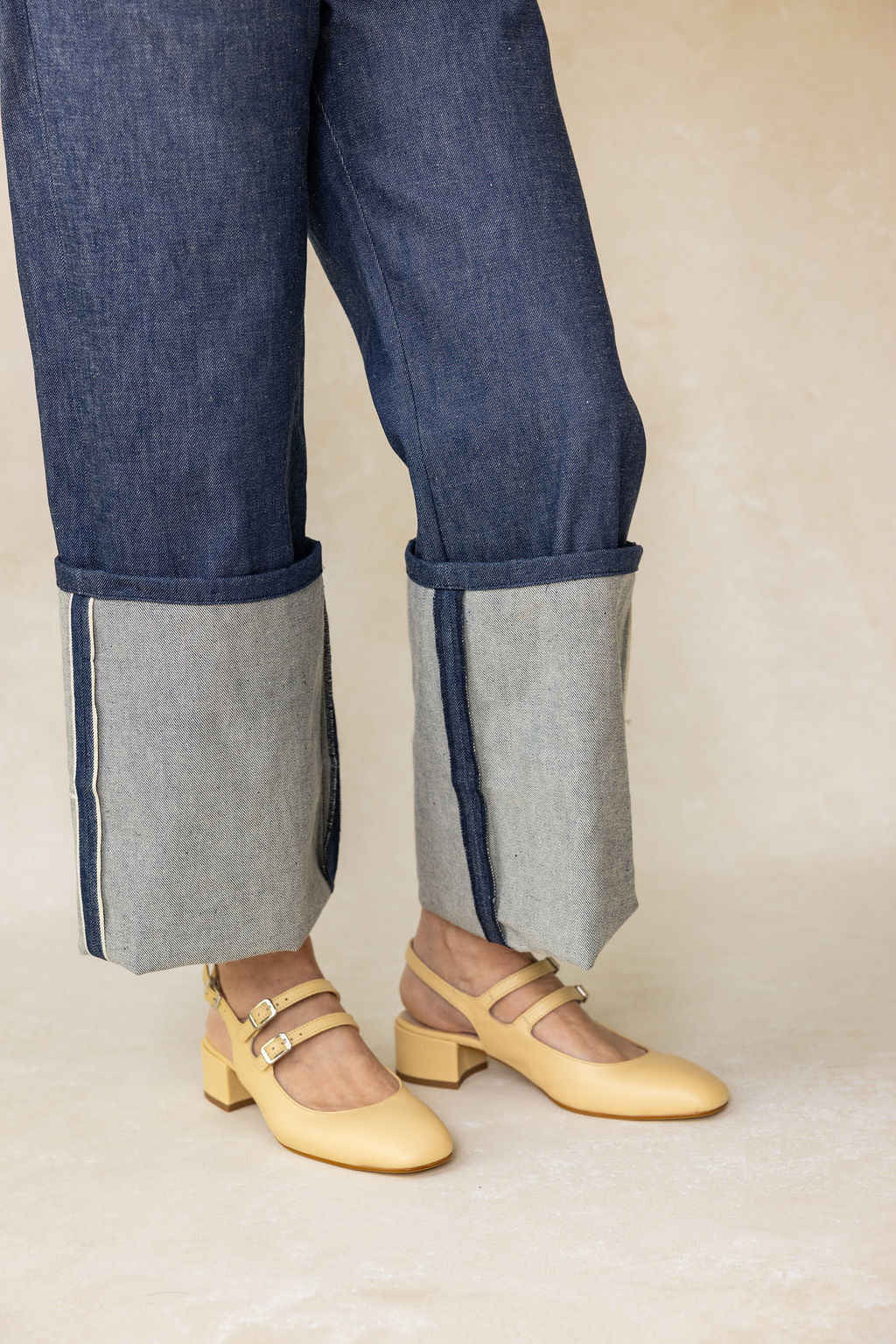 Person wearing blue jeans with gray cuffs and yellow shoes on a beige background