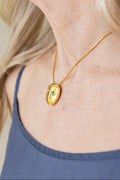 Woman wearing gold chain necklace with a owl-shaped pendant featuring green stones.