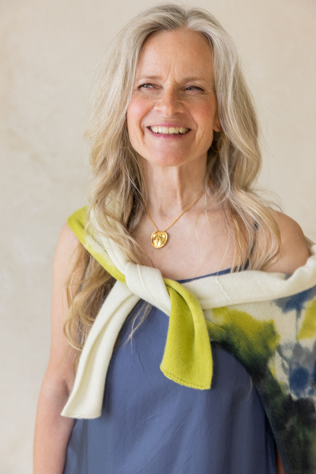 Woman wearing blue dress and cashmere citrine and blue sweater with a gold chain necklace with a owl-shaped pendant featuring green stones.