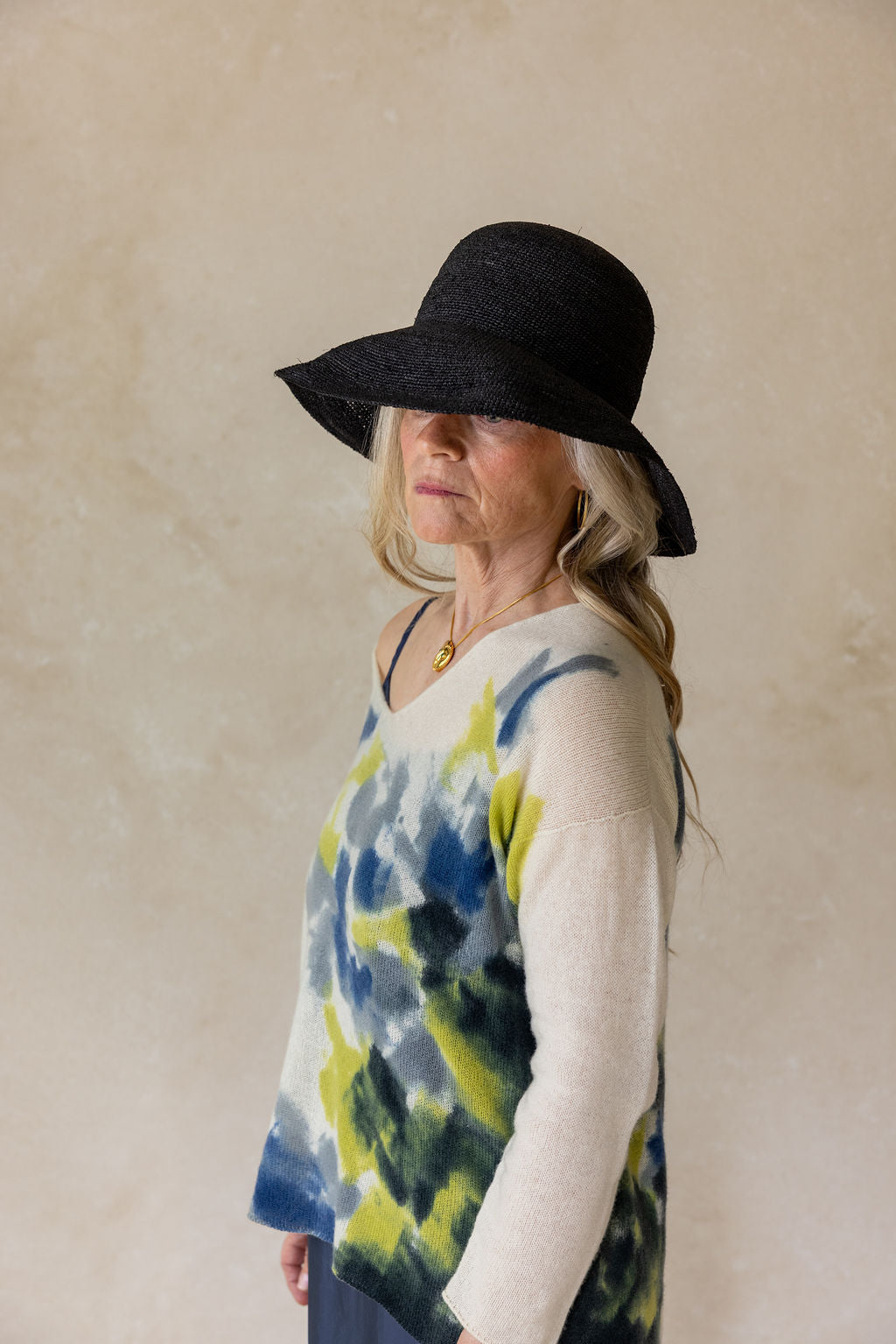 Woman wearing a black hat and tie-dye shirt against a beige background