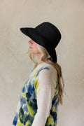 Person wearing a black hat and tie-dye shirt against a plain background