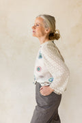 Woman wearing a white blouse with colorful patterns against a beige wall