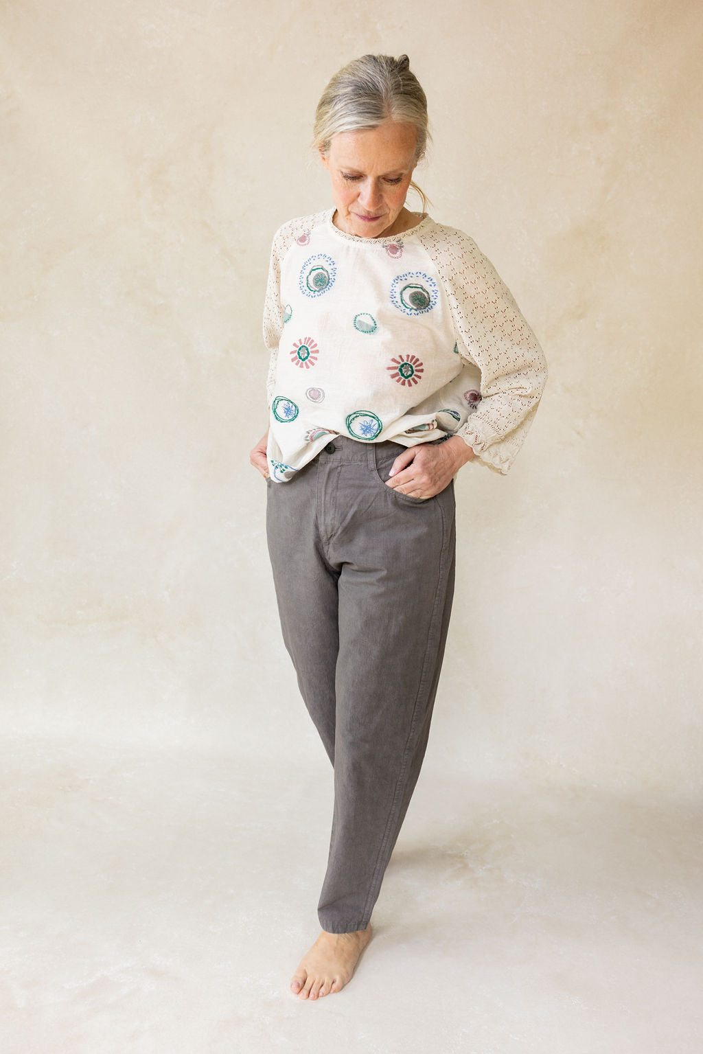 Woman wearing a patterned top and gray pants on a plain background