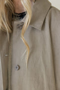 Close-up of a beige trench coat with a person wearing it, focusing on the collar and buttons.