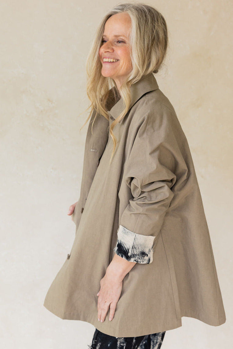 Woman wearing a beige trench coat against a plain background