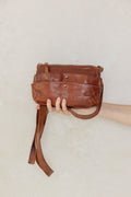 Brown leather bag held by a hand against a light background