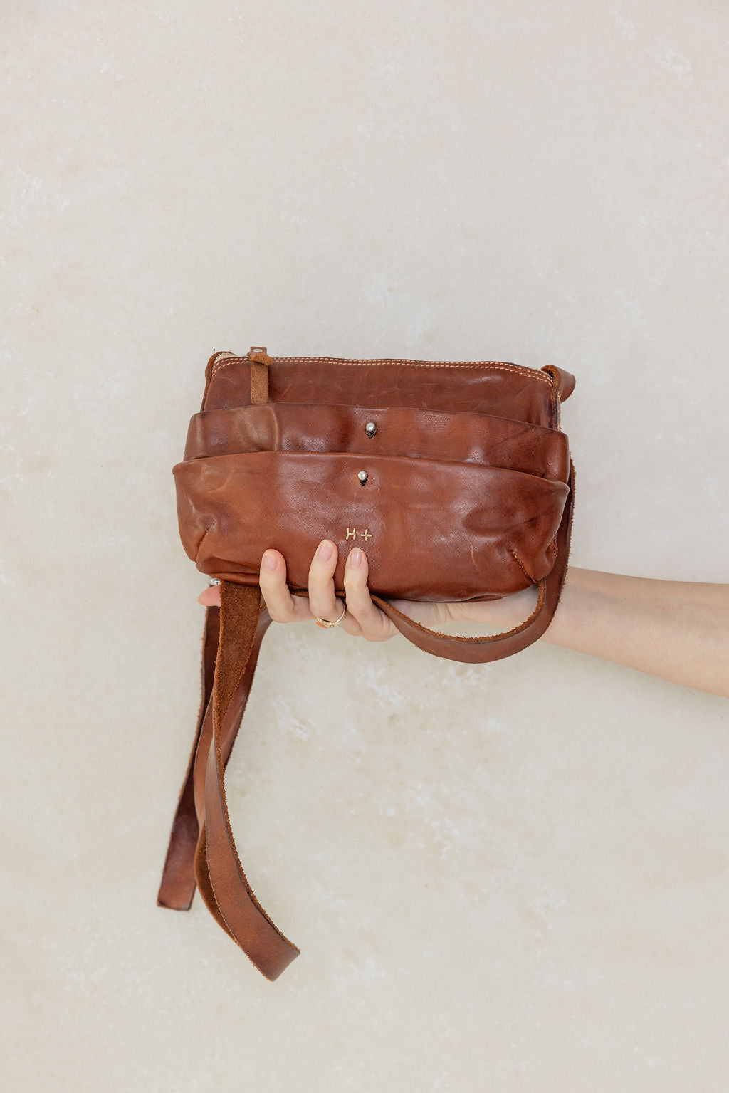 Brown leather bag held by a hand against a light background