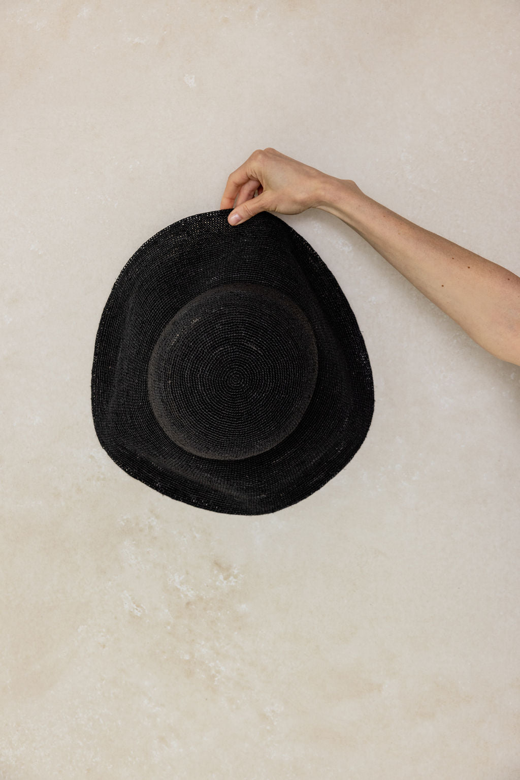 Black straw hat being held by a hand on a light beige background