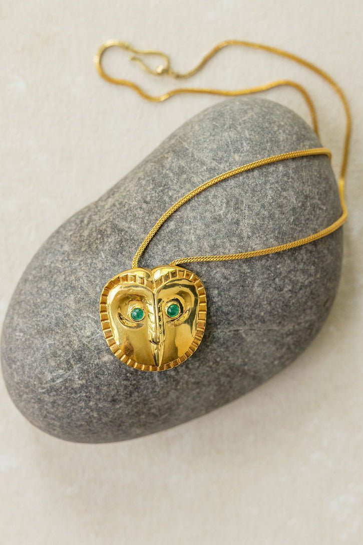 Gold chain necklace with a owl-shaped pendant featuring green stones on a gray stone surface.
