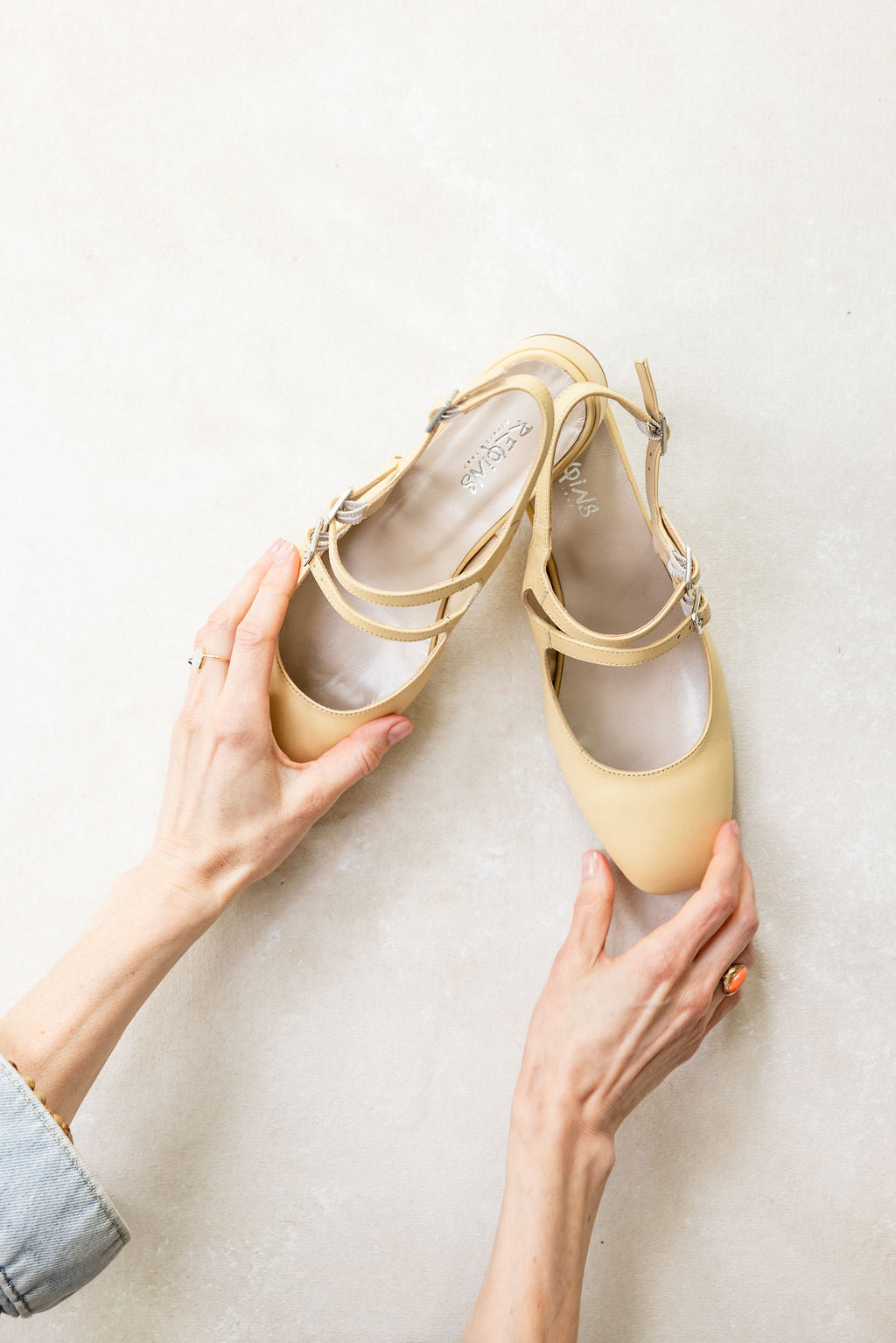 Pair of yellow shoes held by a person against a light background