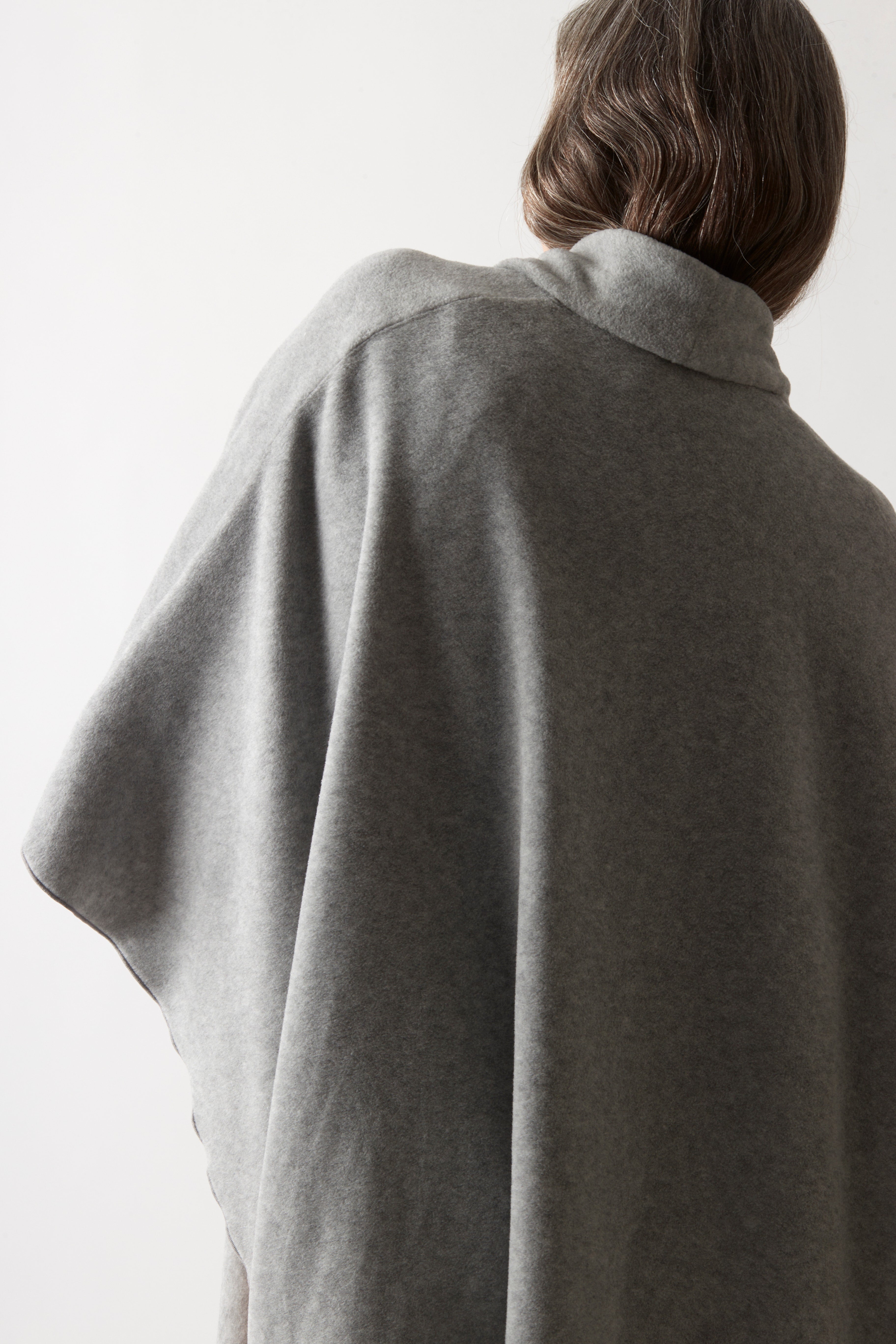 A person shown from behind wearing a draped gray knit poncho or cape against a plain light background.